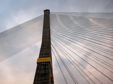 Kablo destekli bir köprünün beton direği, bulutlu bir gökyüzüne karşı arp benzeri bir yapıda kablolarla dizilmiş..