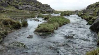 Bulutlu bir gökyüzünün altındaki kayalık arazilerde kristal gibi berrak bir dağ deresi süzülüyor. yakınlaştır