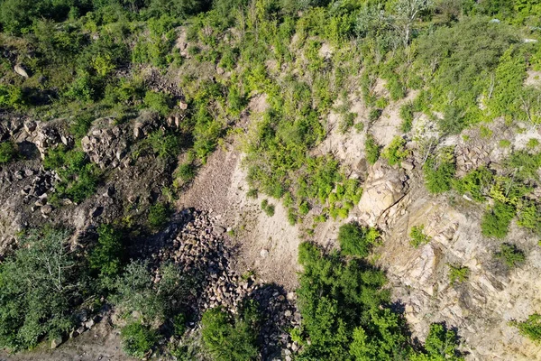 The rocky slopes of the hill are overgrown with bushes and small trees. Rocky terrain, aerial view.