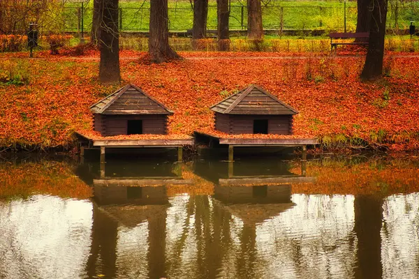 Two duck houses near a pond in Zamosc city park. Autumn landscape.