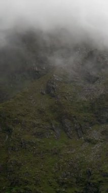 Karamsar atmosferi yükselten kayalık oluşumlarla karakterize edilmiş sisli bir dağ manzarası. Dikey video. pano