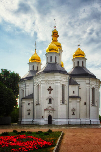 The ancient Orthodox Church of St. Catherine in Chernihiv, with its white facade and iconic golden domes, harmonizing beautifully with the tranquil blue sky.
