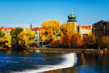 Bu, arka planda şelalesi ve binaları olan bir nehrin fotoğrafı. Sonbaharda nehir kıyısındaki antik kulede. Autumn Prag 'da. Peyzaj.