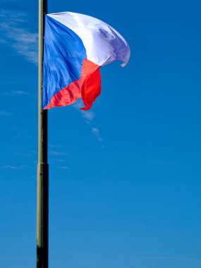 Çek Cumhuriyeti bayrağı, arkasında mavi bir gökyüzü olan bayrak direğinde dalgalanıyor..