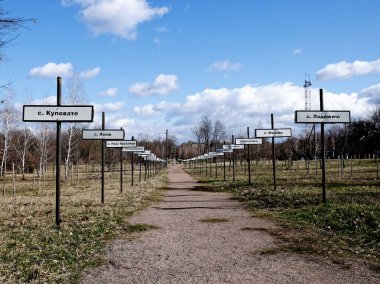 Park benzeri bir ortamda her iki tarafında işaretler olan toprak bir patika. Çernobil nükleer felaketinin yaşandığı bölgedeki terk edilmiş köylerin isimleri. Kiril alfabesindeki köylerin isimlerinin yazılı olduğu iletiler.