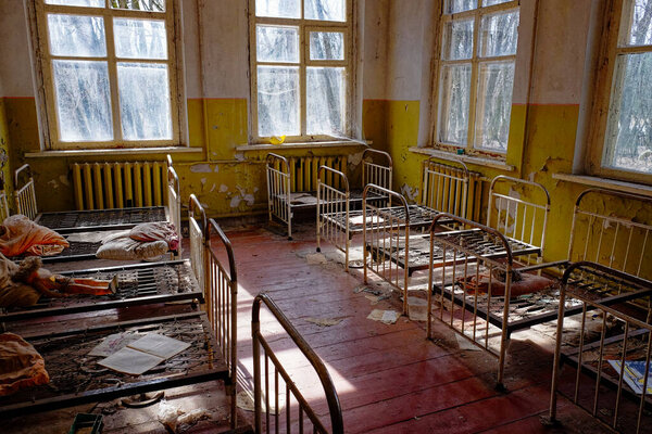 A neglected room with peeling yellow paint and dirty floor. Old childrens beds in an abandoned kindergarten. The interior of a room in one of the buildings in the Chernobyl radioactive exclusion zone.