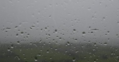 Pencerenin üzerinde çeşitli boyutlarda yağmur damlalarının fotoğrafı var, içeriden çekilmiş. yakınlaştır