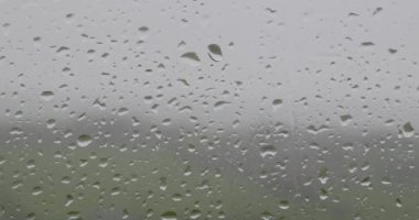 Gri bir günde pencereye düşen yağmur damlalarının videosu. yakınlaştır