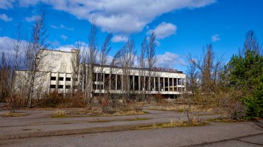 Aşırı gelişmiş bitki örtüsü ve çıplak ağaçlarla çevrili kırık camlı harap bir bina. Energetik Kültür Sarayı, Pripyat 'ta terk edilmiş, çok işlevli bir kültür sarayı..