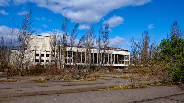 A dilapidated building with broken windows, surrounded by overgrown vegetation and bare trees. The Energetik Palace of Culture is a now abandoned multifunctional palace of culture in Pripyat.