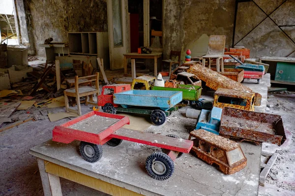 A room with old, rusty toy trucks on a table, surrounded by debris and dilapidated walls.