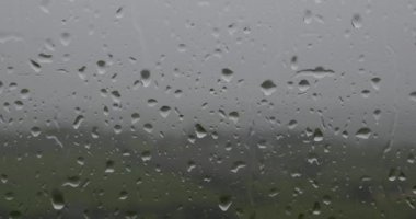 Penceredeki bulanık arkaplanlı yağmur damlalarının peyzaj odaklı videosu. pano