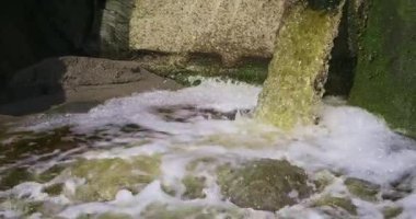 Kaya duvarına gömülü bir borudan köpüklü su fışkırıyor. Ağır çekim. pano