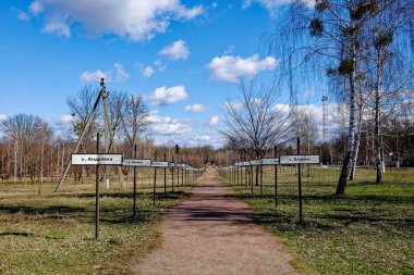 Ağaçlar ve çimlerle kaplı bir patikanın güneşli bir günü. Çernobil nükleer felaketinin yaşandığı bölgedeki terk edilmiş köylerin isimleri. Kiril alfabesindeki köylerin isimlerinin yazılı olduğu iletiler.