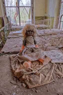 An abandoned room houses a doll with a sad expression. An old doll with a dirty face on a bed in an abandoned kindergarten. Radiation-contaminated room in Chernobyl. clipart