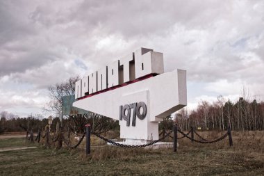 Mavi gökyüzünün altında dağınık bulutlu terk edilmiş bir yapı. Kiril alfabesi ile metin: Pripyat, şehrin adı.