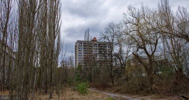 Ormanın arkasında, bulutlu bir gökyüzünün altında eski bir apartman var..