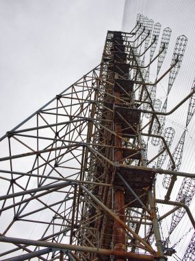 Paslanmış metal yapıları çevreleyen karmaşık tel ağlar. Duga, ICBM fırlatmaları için bir erken tespit sistemi için ufukta görünen bir Sovyet radar istasyonu..