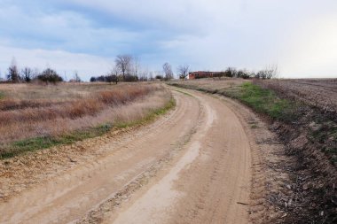 Bulutlu bir gökyüzünün altındaki eve doğru giden toprak bir yol..