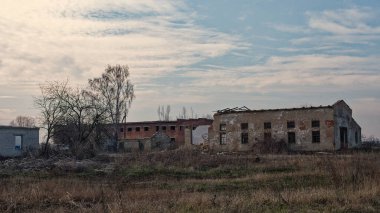 Bulutlu bir gökyüzünün altında kırık camlı harap bir bina..