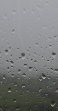 A video of raindrops on a window, with a blurred background of a green field. Vertical video.