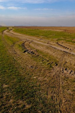 Açık bir çayırın ortasında tekerlek izleri olan kavisli bir patika görülebilir..