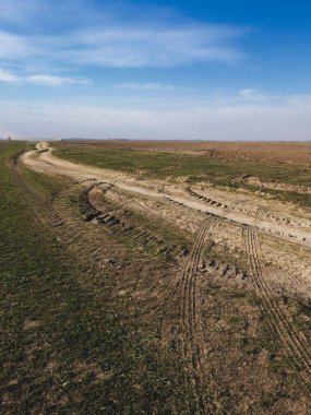 Temiz gökyüzünün altında tekerlek izleriyle işaretlenmiş, virajlı toprak yolu olan boş bir tarla..