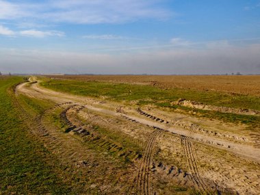 Görüntü huzurlu kırsal bir ortam yakalıyor. Tarlalar ve dolambaçlı bir yol var..