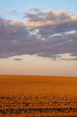 Görüntü, üzerinde bulutlar ve ufuk çizgisi olan kayalık bir arazi gösteriyor..