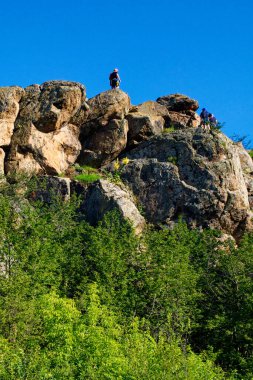 Yeşil gökyüzünün altında insanlarla dolu kayalık bir tepe..