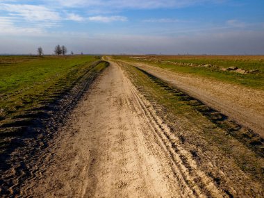 Açık alanlar ve kaldırımsız bir yol açık gökyüzünün arka planına vurgulanır.