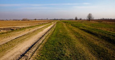 Temiz gökyüzü, eğri bir yol tarafından kesilen açık alanların sakin manzarasına nezaret eder.