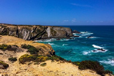 Çalkantılı denizler ve engebeli uçurumlar üzerinde açık gökyüzü.