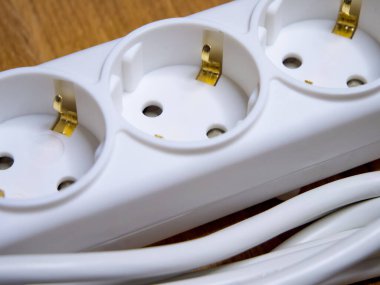 Üç prizli beyaz bir güç şeridi. Şerit ahşap bir yüzeyde..