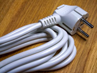 Nizhyn, Ukrayna, 25 Eylül 2021. Ahşap bir masaya kurulmuş iki uçlu fişi olan sarmalanmış beyaz kablo ev ortamlarındaki elektriği sembolize ediyor. İllüstrasyon Editörü.