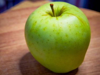 Ahşap bir yüzeyde sapı olan yeşil bir elma, tazeliği ve sağlığı gösterir..