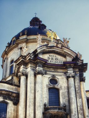 Barok Zarafeti: Açık bir gökyüzünün altında Latince metin ve güneş ışığıyla bir kilise cephesi. Dominik kilisesi ve manastırı.