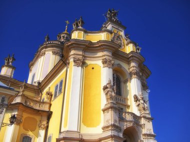 Sunlit Church Exterior: Kültürel mirası sembolize eden, parlak bir günde yakalanan, sanatsal taş işçiliğiyle günışığına çıkarılmış sarı kilise dış görünüşü. Lviv şehrindeki St. George Katedrali