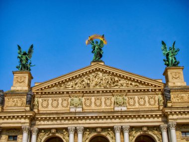 Melek heykelleri. Meleklerin heykelleri, canlı bir gökyüzüne karşı, kültürel ve sanatsal mirası yansıtan, Lviv Opera binasının dış görünüşünü yansıtan klasik bir yapıyı süsler..