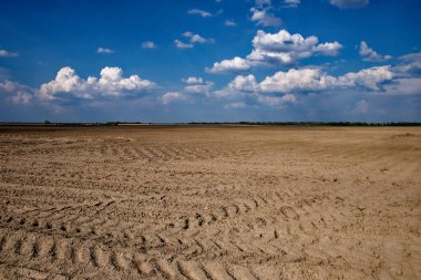 Üstünde toprak ve bulutlar olan boş tarım arazisi.