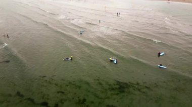 West Cork, İrlanda, 3 Temmuz 2022. Az sayıda kişi sığ ve gri sularda mavi sörf tahtalarının üzerinde duruyor. Su çok sakin. Acemi sörfçüler. Denizdeki eğitmenler ve acemi sörfçüler. Su sporları aktiviteleri.