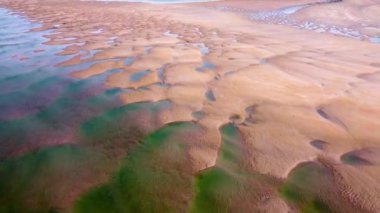 Kumlu deniz yatağı, su çekildikçe, güneş ışığı altında dokuları ve şekilleri ortaya çıkaran ilginç desenleri ortaya çıkarır..
