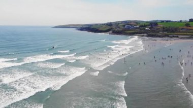 Kalabalık bir plaj ve suda bir tekne. Manzara canlı ve hareketli..