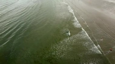 Sahil manzarası, suyun enerjik bir şekilde çalkalanması gibi etrafta gezinen kişilerle dolu..