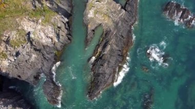 Video, temiz turkuaz suyla çevrili kayalık bir çıkıntıyı gösteriyor. Kayalar koyu gri ve yıpranmış. Su sakin ve berrak, kıyıya yakın dalgalar kırılıyor..