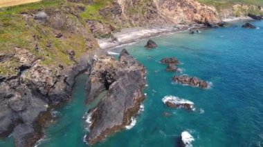 Okyanusun yukarısından bir manzara, berrak mavi suyla kayalık bir kıyı şeridini gösteriyor..