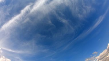 Parlak, mavi bir gökyüzü, ince, beyaz bulutlar yatay olarak sahne boyunca uzanıyor..