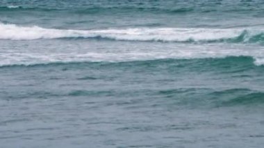 Sakin bir okyanus yüzeyinin yukarıdan aşağıya bakışı. Beyaz köpük tepeli birkaç paralel dalga görülebilir. Su, soluk mavi-yeşil renktir..