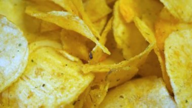 Patates cipsinin yakın çekim görüntüsü. Cipsler altın rengi kahverengidir ve hafif yağlı parıltıları vardır. Bazı cipslerde az miktarda yeşil baharat var..