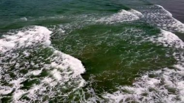 Deniz manzarası, beyaz köpük ve yeşilimsi su deseni sergiliyor. Dalgalar görülebilir, dalgalı bir yüzey dokusu yaratıyor..